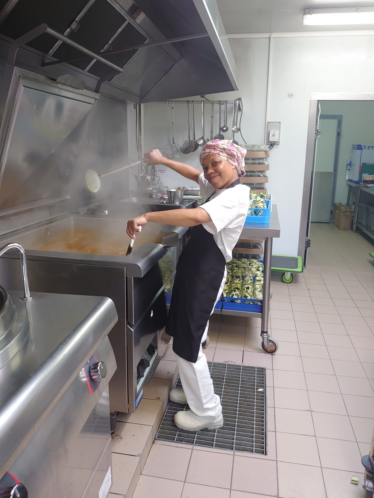 Cuisinière devant cuit vapeur de restauration collective, souriante